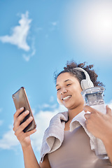 Image showing Headphones, phone and woman with water bottle outdoors streaming music, radio or audio. Social media, networking and low angle of female on 5g mobile or text message after training or running workout