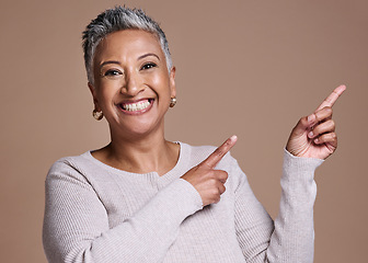 Image showing Woman, smile and happiness in studio for advertising free space, promo or mockup on a brown background for cosmetics, makeup or fashion. Face portrait of a mature model pointing finger at mock up