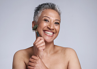 Image showing Woman, roller and face for skincare beauty, health or exfoliate for cosmetic wellness by wall. Happy, senior model and crystal for dermatology massage, cosmetics or glow on skin by studio background