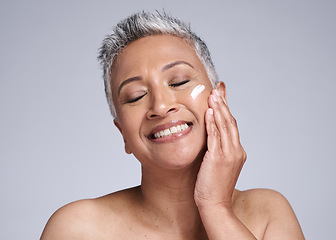 Image showing Face, skincare and beauty with a senior woman using cream for antiaging treatment in studio on a gray background. Cosmetics, lotion and cosmetology with a mature female applying cream to skin