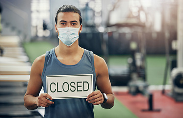 Image showing Covid, gym and man holding closed sign during the pandemic while wearing a face mask. Coronavirus, health center and quarantine lockdown with fit, strong male in empty gymnasium