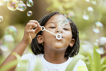 Image showing Bubbles, playful and African girl in nature with freedom, smile and playing in a park. Spring, happy and carefree child with a bubble game in a backyard or field with plants for happiness and youth