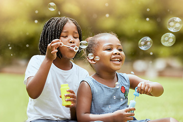 Image showing Black kids, children and blowing bubbles at park, having fun and bonding. Girls, happy sisters and playing with soap bubble toys, relax and enjoying garden together outdoors in nature on grass