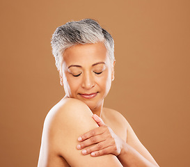 Image showing Face, skincare and senior woman with eyes closed in studio on a brown background. Aesthetics, makeup and cosmetics of mature female model from India touching skin or arm for healthy skincare routine.