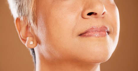 Image showing Face, lips and beauty with a mature woman in studio on a brown background to promote cosmetics. Mouth, skincare and wellness with a senior female model posing for natural skin or lip treatment