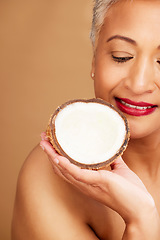 Image showing Beauty, skincare and coconut with a senior woman in studio on a brown background to promote natural antiaging care. Cosmetics, moisture and hydration with a mature female posing with a fruit half