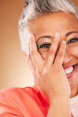 Image showing Makeup, comic and senior woman creative with color for face against a brown studio background. Playful, happy and hand of an elderly model with facial cosmetics for creativity, beauty and fashion
