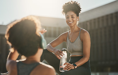 Image showing Fitness, headphones and black women or friends in city on break with water bottle and talking. Health, wellness and people resting while streaming music, radio or podcast after running or training.