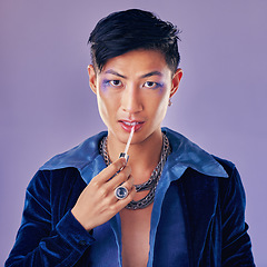 Image showing Fashion, beauty and makeup with a man model in studio on a purple background applying red lipstick. Face, portrait and cosmetics with a young asian male indoors to promote a cosmetic product