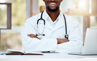 Image showing Healthcare, stethoscope and doctor with crossed arms at desk for support, consultation and wellness. Medicine, medical worker and black man sitting in hospital or clinic with smile, laptop and book