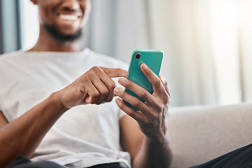 Image showing Hands, phone and social media with a black man typing a text message while sitting on a sofa in his home. Mobile, communication and networking with a male chatting from the living room in his house