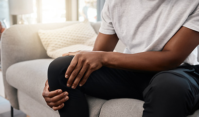 Image showing Knee pain, hand of a man and injury while sitting on home living room sofa for rest and relaxation. Ache, painful leg joint and african american man touching his knees for a strain muscle