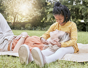 Image showing Mother, picnic and happy child in a interracial family with a smile, floor hug and happiness. Summer fun, adoption and love of mom and girl on a vacation feeling relax in a garden field outdoor park