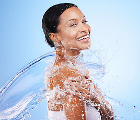 Image showing Woman, skincare and water splash, happy and cleaning body, hygiene and shower against blue studio background. Cleaning, health and luxury with happy model for cosmetics, hydration and dermatology