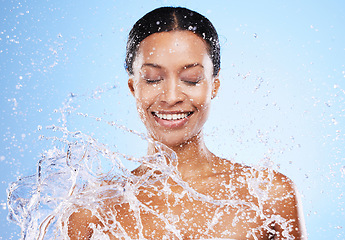 Image showing Water splash, shower and washing with a black woman in studio on a blue background for hygiene or hydration. Bathroom, happy and cleanliness with a young female model washing his skin for fresh care