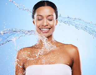 Image showing Woman, water splash and shower with body cleaning and smile with healthy skincare in blue studio background. Clean, face and water splash with an attractive young female cleaning in the bathroom