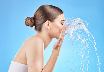 Image showing Skincare, water and woman cleaning face in studio on blue background for wellness, hygiene and facial cleanse. Beauty, hydration and girl washing skincare products, cosmetics and makeup with splash