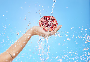 Image showing Water, wellness and hand with pomegranate in studio on blue background for nutrition, diet and healthy lifestyle. Beauty, spa and person holding fruit for skincare products, cosmetics and luxury