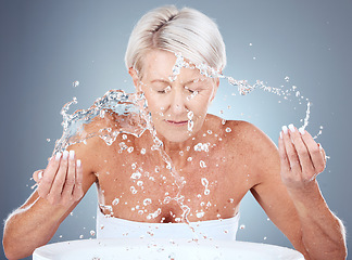 Image showing Senior woman, water splash and skincare with cleaning, wellness and face wash against a grey studio background. Elderly model, beauty and facials washing with liquid, hands and beauty treatment