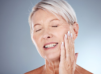 Image showing Elderly woman, hand and smile for skincare, cosmetics or moisturizer against a grey studio background. Senior female touching face and smiling in satisfaction for healthy anti aging facial treatment