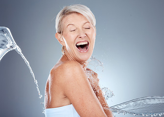 Image showing Water splash, health and portrait of senior woman shocked and surprised on gray background. Skincare, wellness and beauty, a happy mature lady splashed with water with happy smile on face in studio.