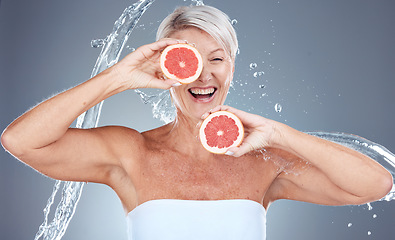 Image showing Grapefruit, water and senior woman with a splash for skincare, beauty and wellness against a grey studio background. Water splash, health and excited elderly model with fruit for diet lifestyle