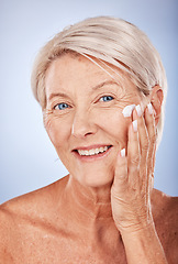 Image showing Portrait, skincare and senior woman with face cream for moisturizing on blue studio background. Beauty, smile or elderly female model apply facial creme, cosmetics product or lotion for healthy skin