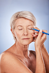 Image showing Eyeliner, makeup and senior woman with beauty against a grey studio background. Cosmetic, color and elderly model with focus while applying cosmetics to face and eyelid with pencil during retirement