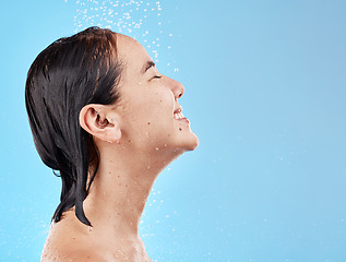 Image showing Asian woman, shower and water for cleaning, smile and happy in blue studio mockup background. Model, clean and showering face, body and hygiene, skincare or cosmetic beauty in bathroom with happiness