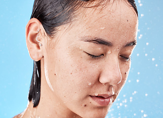 Image showing Calm, water and woman in the shower for grooming, hygiene and relax against a blue studio background. Cleaning, skincare and Asian model relaxing during body care for wellness, beauty and routine