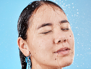 Image showing Relax, water and face of a woman in the shower for cleaning, peace and health against a blue studio background. Skincare, wellness and Asian model with hair care, beauty and natural self care