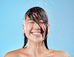 Image showing Shower, woman and water with a face cleaning for clean, wash and hygiene on a blue studio background. Bathroom, showering and asian female cleansing her body for health and wellness in studio