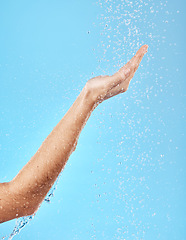 Image showing Hand, shower and water for skincare hygiene, wash or dermatology against a blue studio background. Arm and hands of person in healthy wellness, skin hydration and washing for body care treatment