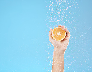 Image showing Hand, orange and water with natural skincare for health, wellness and organic fruit on a blue studio background. Beauty, fresh and food for juicy vitamin c skin care treatment for dermatology