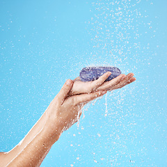 Image showing Shower, soap and woman hands in a studio to wash her hands or body for hygiene, wellness or health. Water, clean and closeup of model holding soap bar for self care while isolated by blue background.