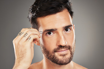 Image showing Face, portrait and tweezers with a man model plucking his eyebrows in studio on a gray background. Skincare, wellness and luxury with a handsome young male tweezing his eyebrow hair for grooming