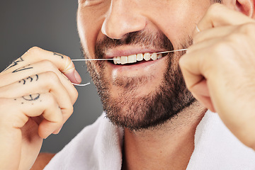 Image showing Floss, dental hygiene and man cleaning teeth, for wellness and against grey studio background. Oral health, healthy male and thin filaments string for fresh breath, remove plaque and mouth healthcare