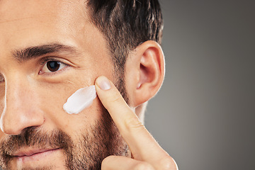 Image showing Face, skincare and beauty with a man model using treatment in studio on a gray background for wellness. Finger, cosmetics and antiaging with a handsome young male inside to apply lotion to his cheek