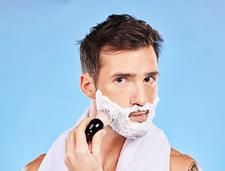 Image showing Face, shave and grooming with a man model shaving his skin for hair removal in studio on blue background. Portrait, brush and hygiene with a handsome young male in the bathroom for a morning routine