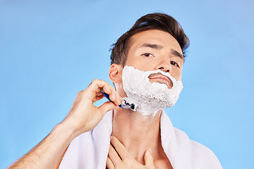 Image showing Portrait, shave and bathroom with a man model shaving his face in studio on a blue background for grooming. Beauty, skincare and shaving foam with a handsome young male using a razor in the morning