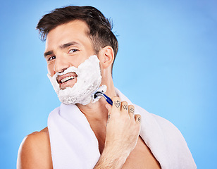 Image showing Face, shave and hair removal with a man model shaving his skin in studio on a blue background for wellness or hygiene. Portrait, beard and razor with a young male grooming alone in the bathroom