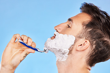 Image showing Shave, cream and man grooming his beard with a shaver in studio for health, skincare and hygiene. Foam, razor and model shaving his facial hair for a face or skin routine isolated by blue background.