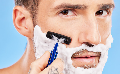 Image showing Grooming, cream and man shaving his face with a razor for wellness, skincare and health against a blue studio background. Beauty, young and portrait of a model with foam on beard for hygiene