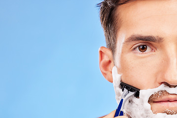 Image showing Face, shave and grooming with a man model shaving his beard in studio on a blue background with mockup. Portrait, closeup and razor with a handsome young male in the bathroom for hair removal