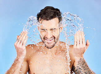 Image showing Face, water and cleaning with a man model splash in studio on a blue background for hygiene. Skincare, water splash and hydrate with a handsome young male washing his skin in the bathroom for care