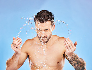 Image showing Face, water and splash with a man cleaning his skin in studio on a blue background for hygiene or hydration. Wellness, skincare and water splash with a handsome young male washing his body for care