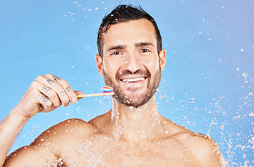 Image showing Shower, brushing teeth and hygiene with a man model in studio on a blue background with splash for oral care. Water, cleaning and dental with a handsome young male wet in the bathroom for wellness