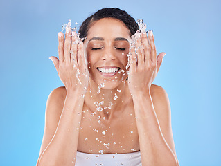 Image showing Skincare, water and woman washing face for clean, healthy and natural wellness against a blue studio background. Beauty, cleaning and happy model with splash for facial satisfaction and routine