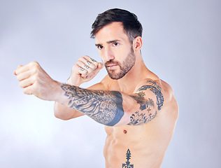 Image showing Man, boxing and punching on studio background in fitness workout, body training or exercise for competition fight, anger management or stress control. Boxer, sports athlete and mma model with tattoos