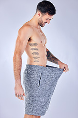 Image showing Motivation, diet and weight loss, man checking pants size change from workout and healthy lifestyle on studio background. Fitness, nutrition and wellness, balance in body care, male model with tattoo